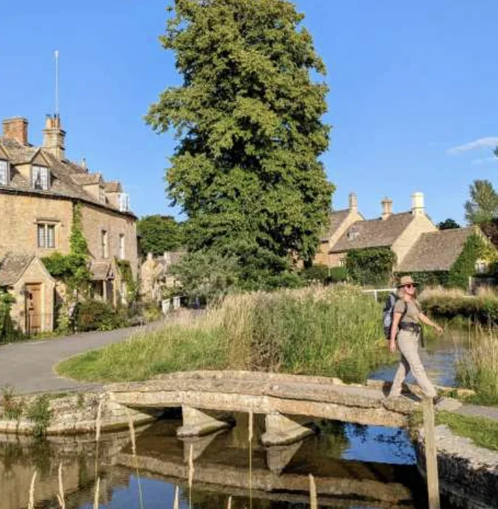 Walker crossing a stone bridge in a Cotswold village