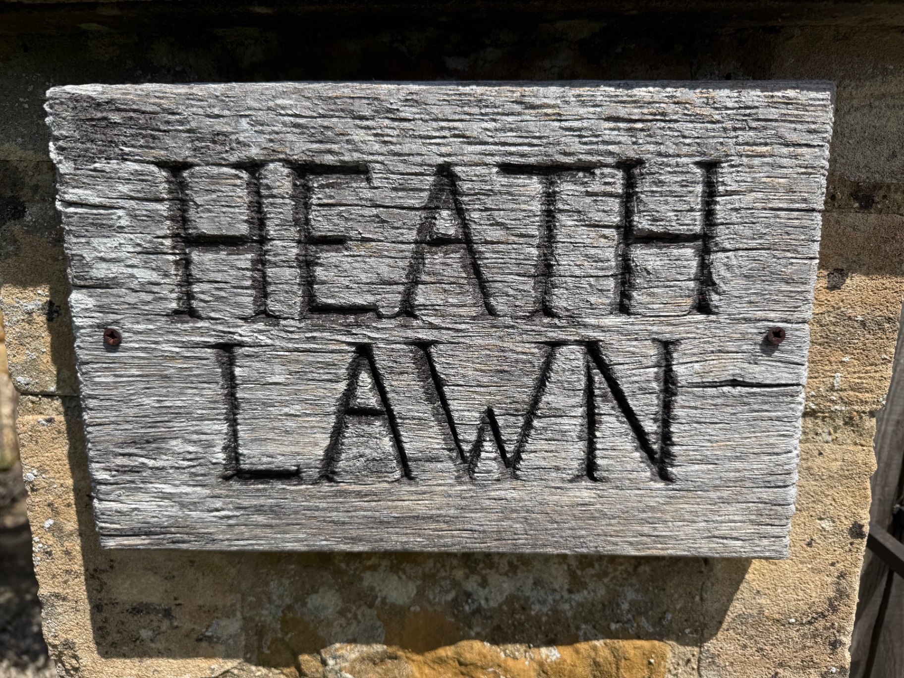 Weathered wooden 'Heath Lawn' name sign carved into oak